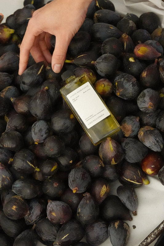 Mano tomando el Aceite Hidratante de higo, vetiver y hoja de laurel de Laguna Cyprien sobre una cama de higos negros frescos.