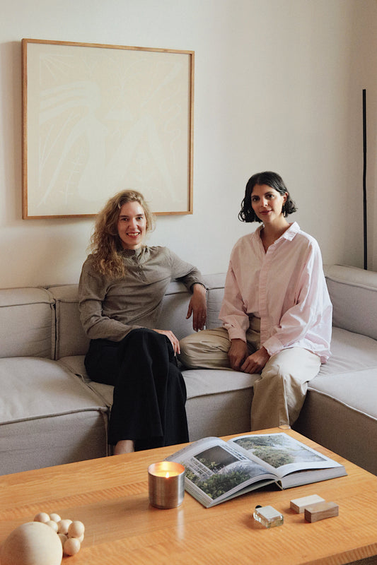Katarina y Maria, socias de Laguna Cyprien, sentadas en el sillon en una sala, con una vela laguna cyprien prendida.