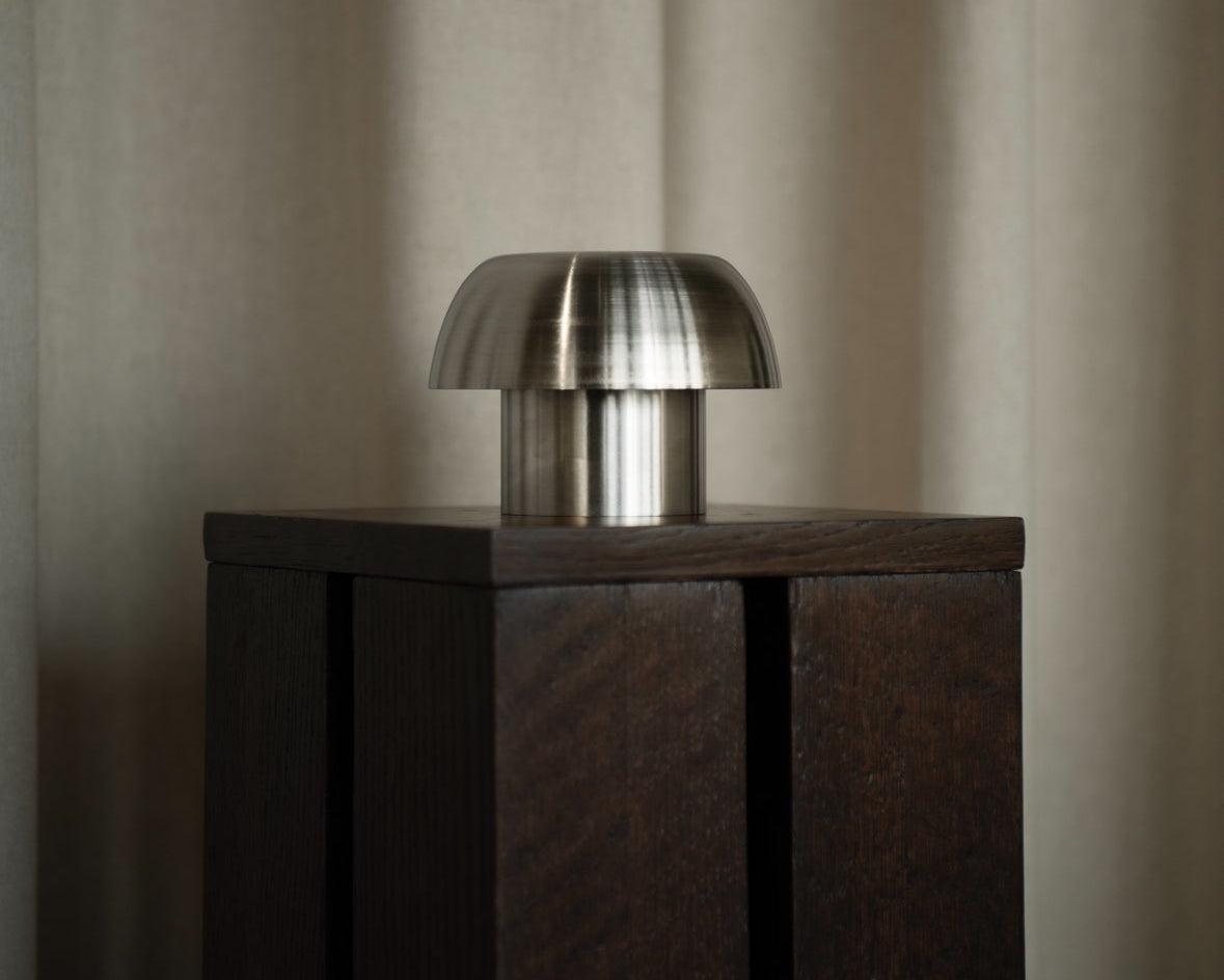 Difusor aromático Laguna Cyprien, pequeño, sobre un pedestal oscuro frente a unas cortinas de color beige. Diseño minimalista.