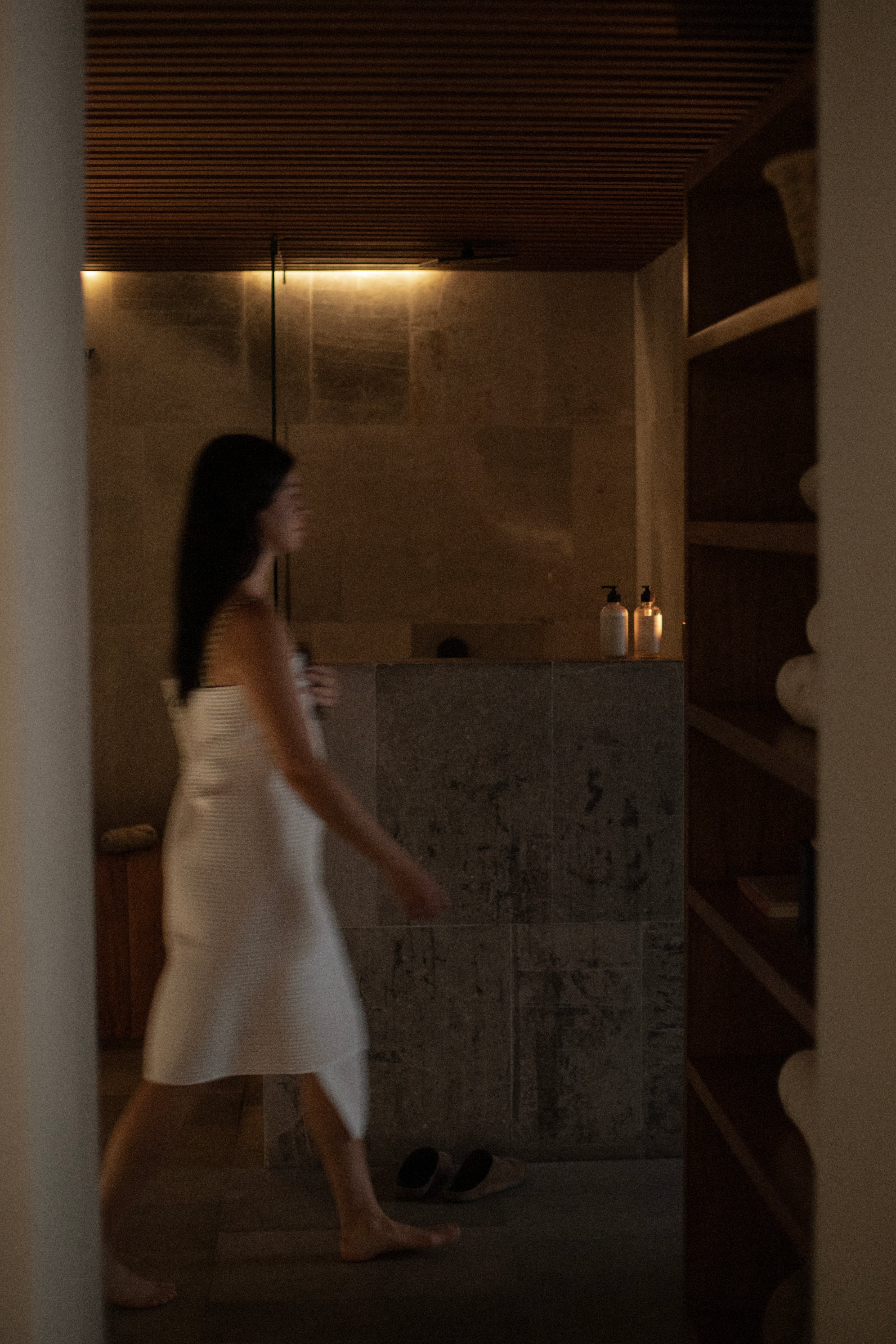 Un baño de un hotel con diseño y estético acompañado de un huésped caminando con una toalla de algodón.