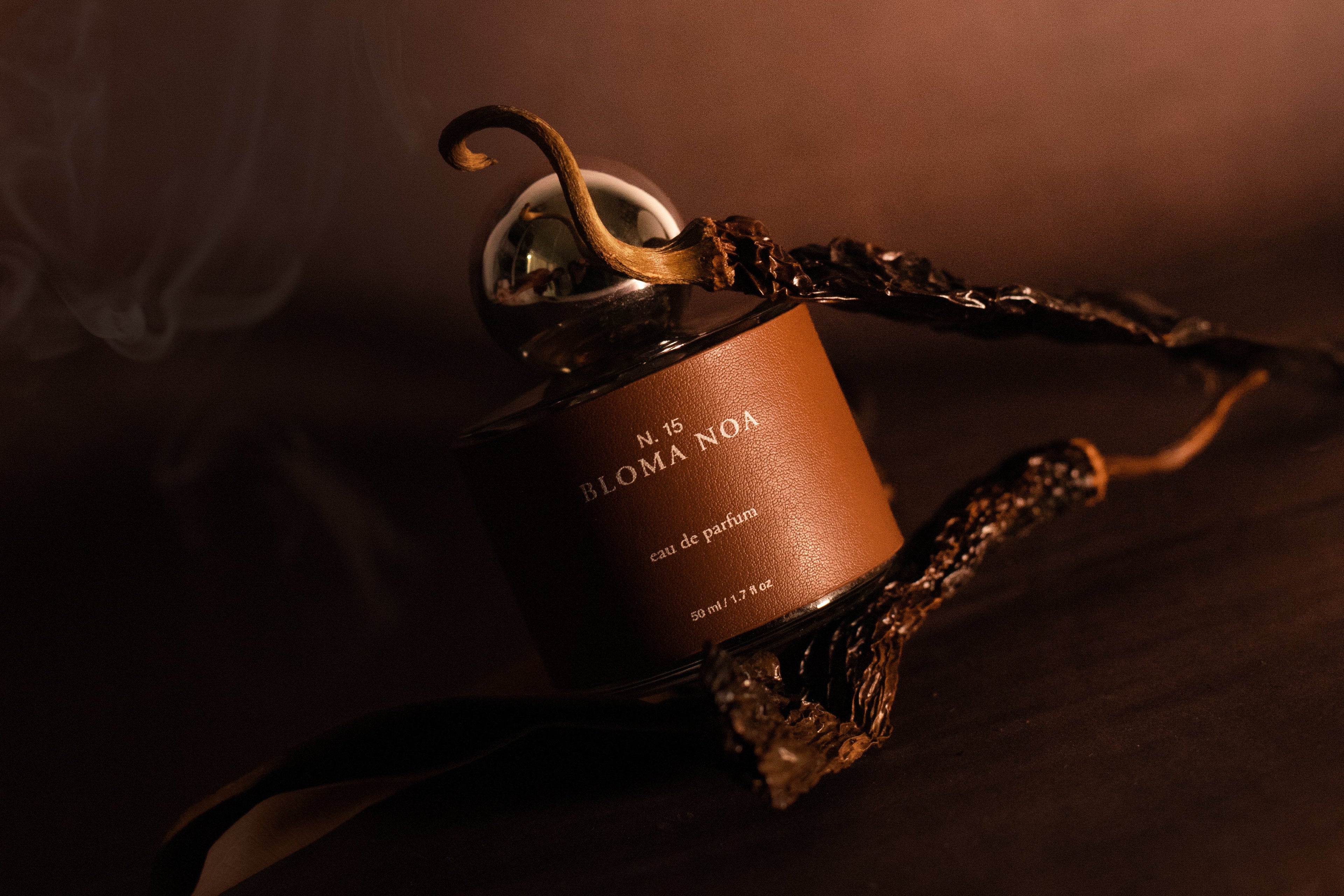 Perfume Bloma Noa de Laguna Cyprien con estética cálida y ahumada, botella de fragancia artesanal sobre superficie en tonos terracota con humo envolvente, inspirado en la fuerza femenina y raíces mexicanas